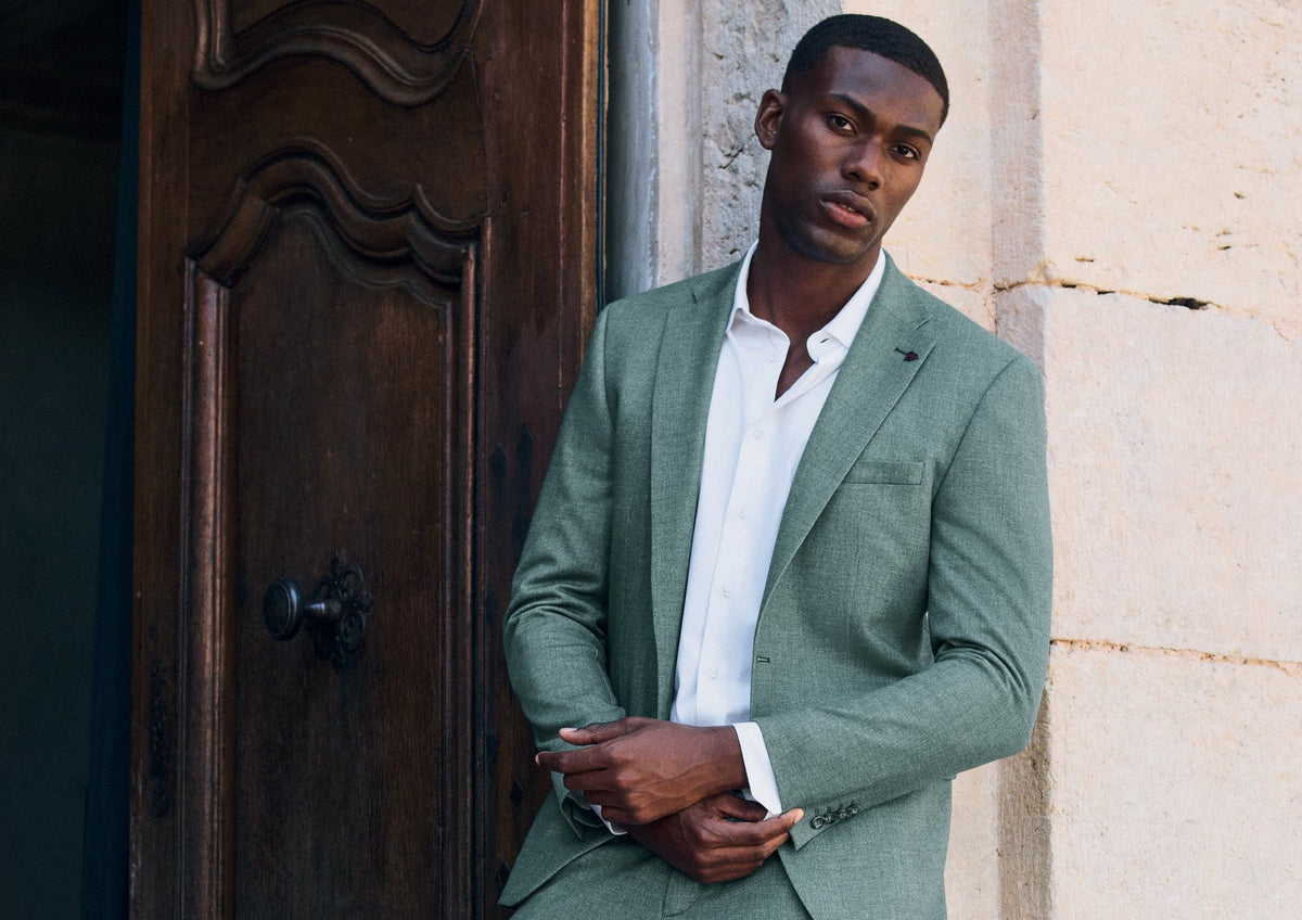 Homme en costume vert clair devant une porte ancienne